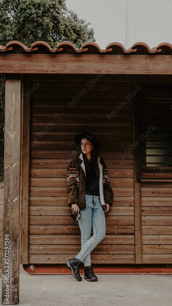 Isolated beautiful girl wearing a hat and with the camera in one hand waiting in a cabin in the woods
