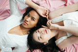 Asian and african women in white shirt laying on pink cloth.