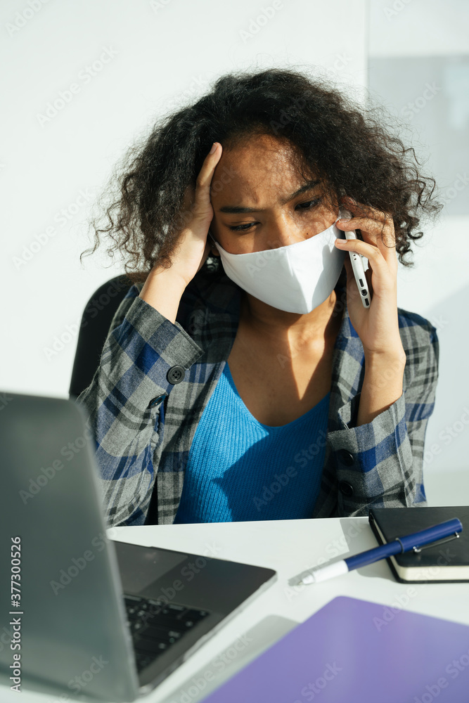 © THESHOTS.CO - Busy african business woman wear mask talking on the phone.