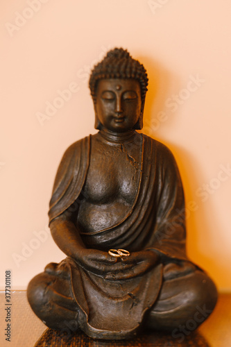 Gold rings of the bride and groom for the wedding on the hands of a Buddha figurine.