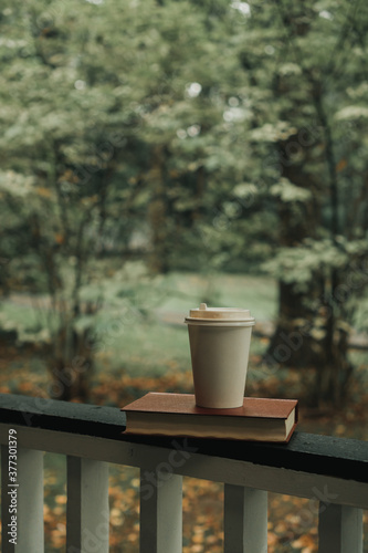 a coffee mug stands on a wooden handrail in an autumn park. An autumn leaf lies nearby
