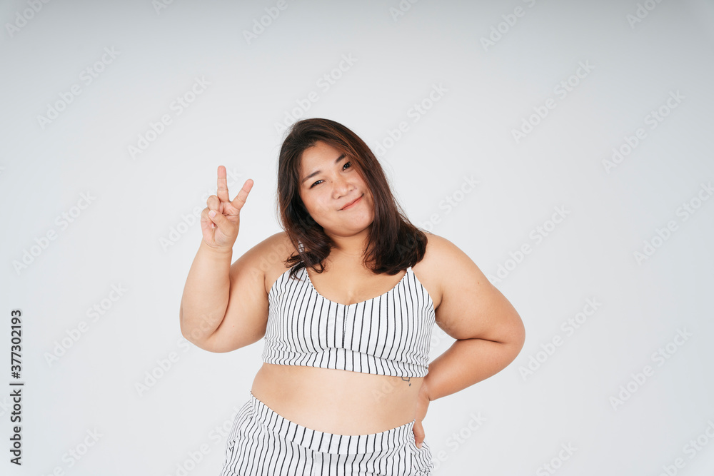 Asian fat woman in white sport bra showing two fingers victory gesture isolate over white background. Asian fat woman in white sport bra showing two fingers victory gesture isolate over white background.