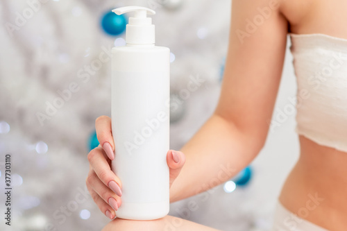 Cosmetics white bottle in hand of young female on christmas tree background. Concept of New Year discounts