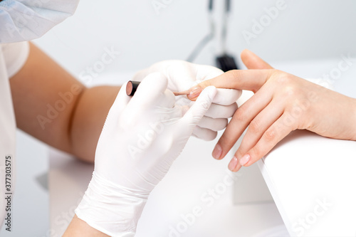 Manicure master in protective gloves applying beige nail polish on female nails in beauty salon photo