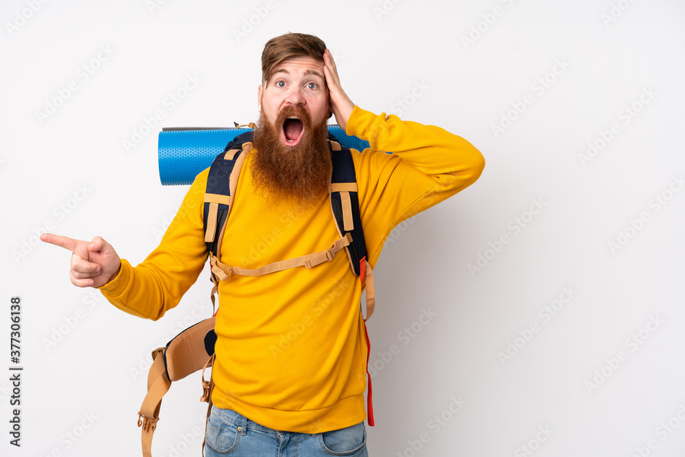Young mountaineer man with a big backpack over isolated white background surprised and pointing finger to the side Young mountaineer man with a big backpack over isolated white background surprised and pointing finger to the side