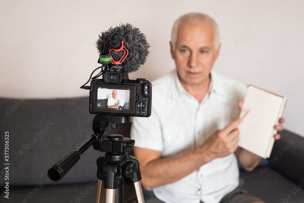 Mature grey heared professor making a video for lecture at home using video camera, online education