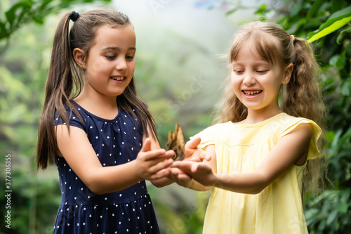Two little sisters holding a butterfly in their hands. Children exploring nature. Family leisure with kids at summer.