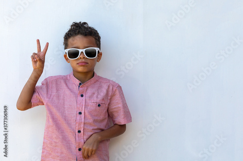 Adorable Mixed Race Boy making peace sign with eyes hidden behind sunglasses