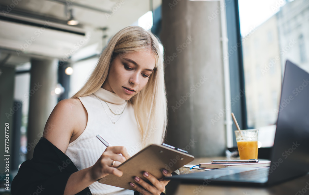 © BullRun - Concentrated woman writing on clipboard in cafe