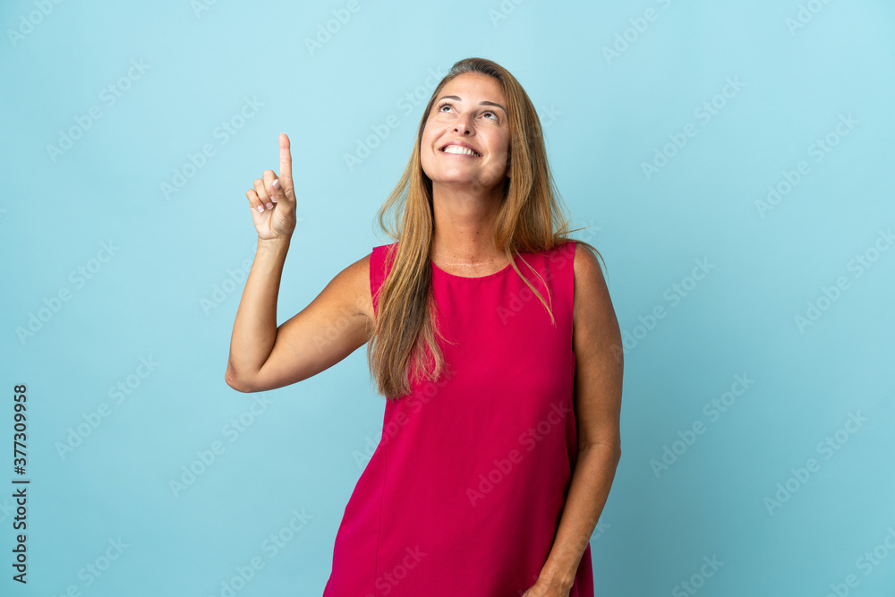 Fototapeta premium Middle age brazilian woman isolated on blue background pointing up and surprised