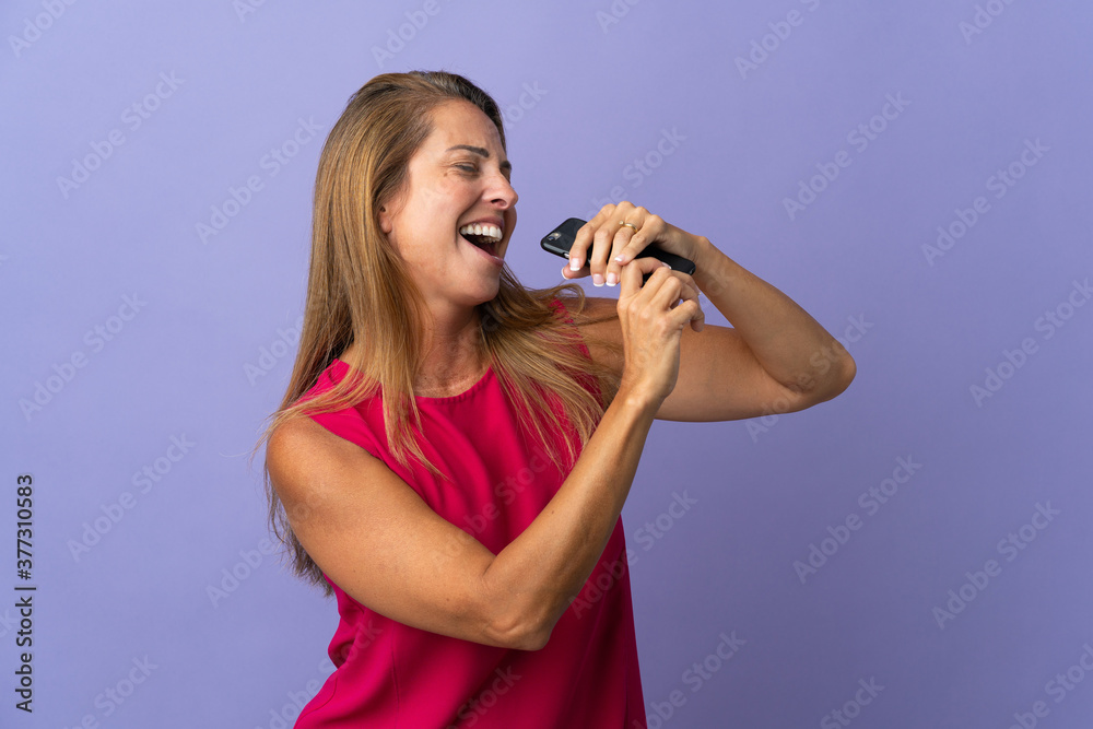 Middle age brazilian woman isolated on purple background using mobile phone and singing Middle age brazilian woman isolated on purple background using mobile phone and singing