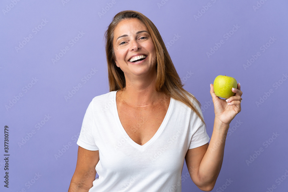 Middle age brazilian woman isolated on purple background with an apple and happy Middle age brazilian woman isolated on purple background with an apple and happy
