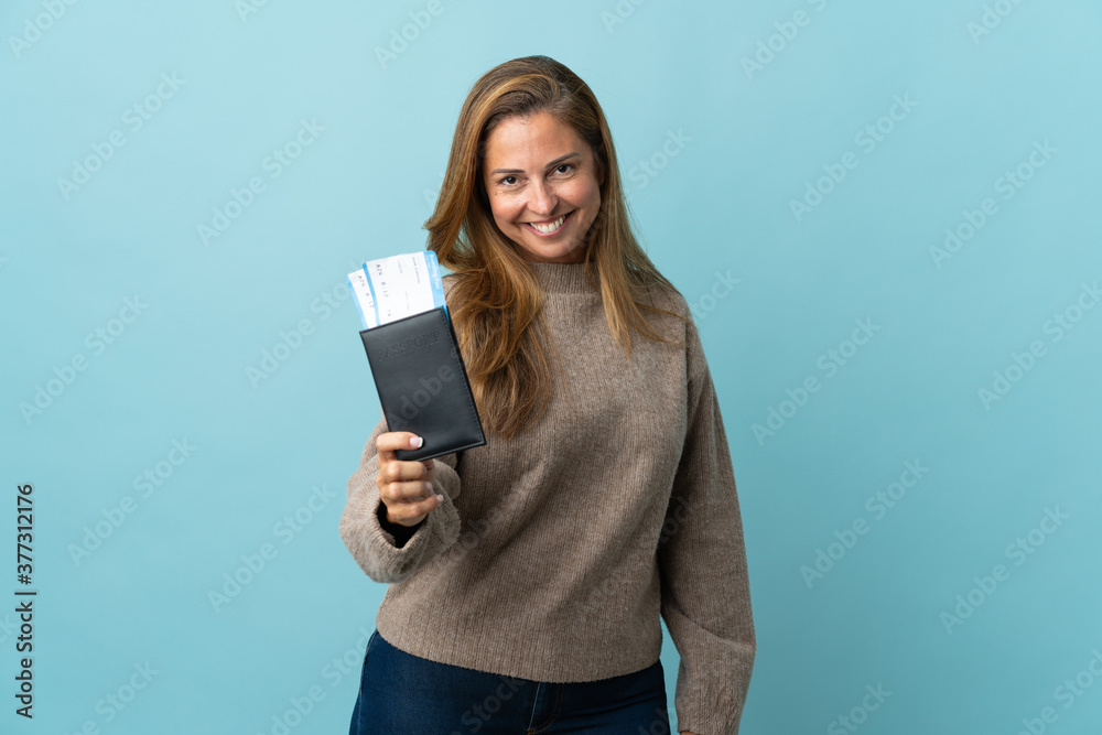 Naklejka premium Traveler middle age woman holding a suitcase isolated on blue background happy in vacation with passport and plane tickets