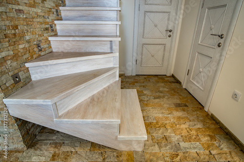 Stylish wooden contemporary staircase inside loft house interior. Modern hallway with decorative limestone brick walls and white oak stairs.