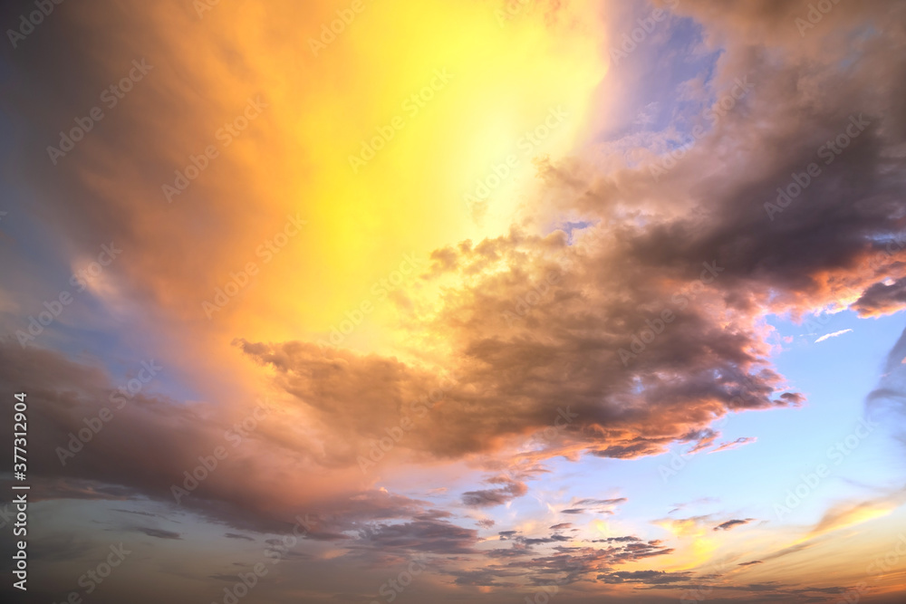 Fototapeta premium Dramatic cloudy sunset landscape with puffy clouds lit by orange setting sun and blue sky.