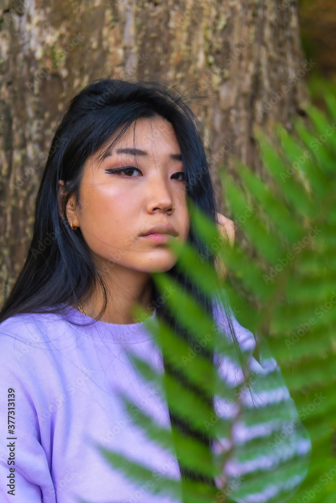 Portrait of a young Asian brunette in a park next to a tree and a fern leaf near her face. Lifestyle, portrait Asian girl Portrait of a young Asian brunette in a park next to a tree and a fern leaf near her face. Lifestyle, portrait Asian girl