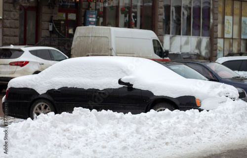Cars parked on a side of city street covered with snow in winter.