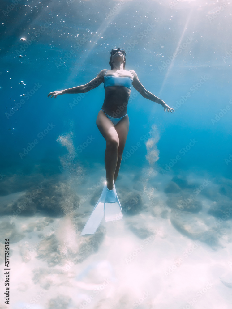 Freediver woman glides and posing over sandy sea with white freediving fins.