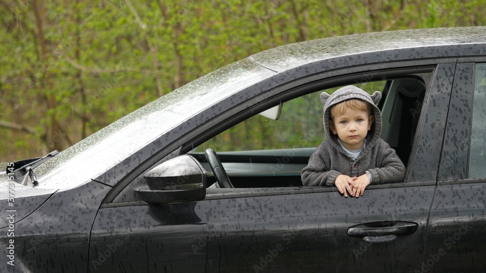 Cute little child at car window smiling, spring rainy day Cute little child at car window smiling, spring rainy day