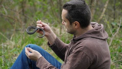 Fotografie Man sitting on grass and holding a snake, love herpetology
