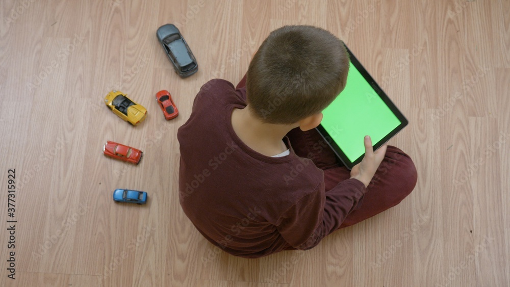 © MEDIAIMAG - Child sit on floor and search on green screen tablet, boy let cars toys apart , early modern technology addiction © MEDIAIMAG - Child sit on floor and search on green screen tablet, boy let cars toys apart , early modern technology addiction