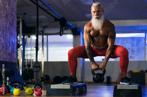 Senior fitness man doing kettle bell exercises inside gym - Fit mature male training in wellness club center - Body building and sport healthy lifestyle concept