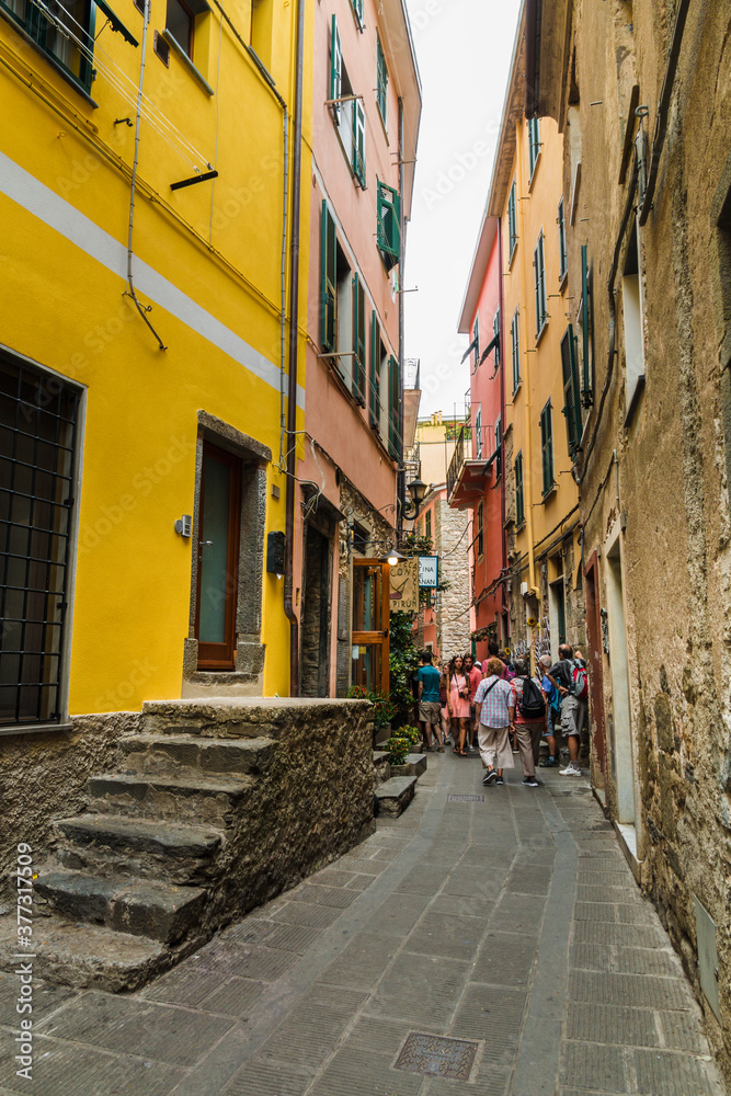 Tourists walking through the narrow main road Via Fieschi with colourful houses on each side in the ancient village Corniglia at the coastal area of Cinque Terre, Liguria, Italy.