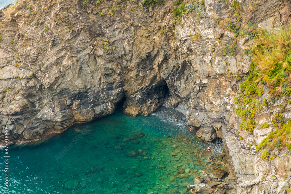 Great close-up view of the small cove near the Corniglia Marina. A couple in bathing gear is trying to reach the rocky bay with its beautiful shallow turquoise blue water.