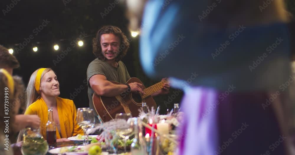 Joyful mixed-race young people having fun at party in garden in evening. Happy Caucasian male playing the guitar and singing outdoor. Pretty African American girl with smile on face. Leisure concept Joyful mixed-race young people having fun at party in garden in evening. Happy Caucasian male playing the guitar and singing outdoor. Pretty African American girl with smile on face. Leisure concept