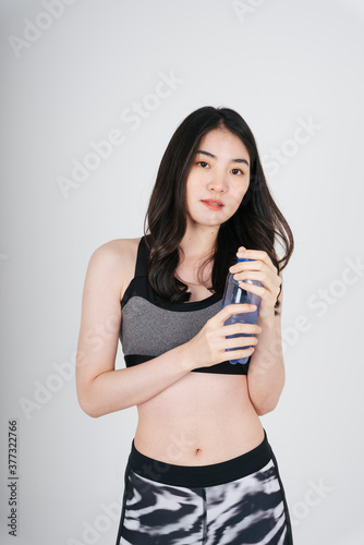 Asian woman in sport bra outfit holding water bottle on white background.