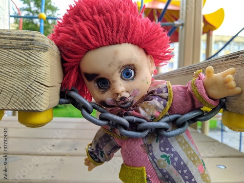 scary toy a clown with blue eyes and red hair behind a chain that holds it will take you with him beckoning with his hand photo