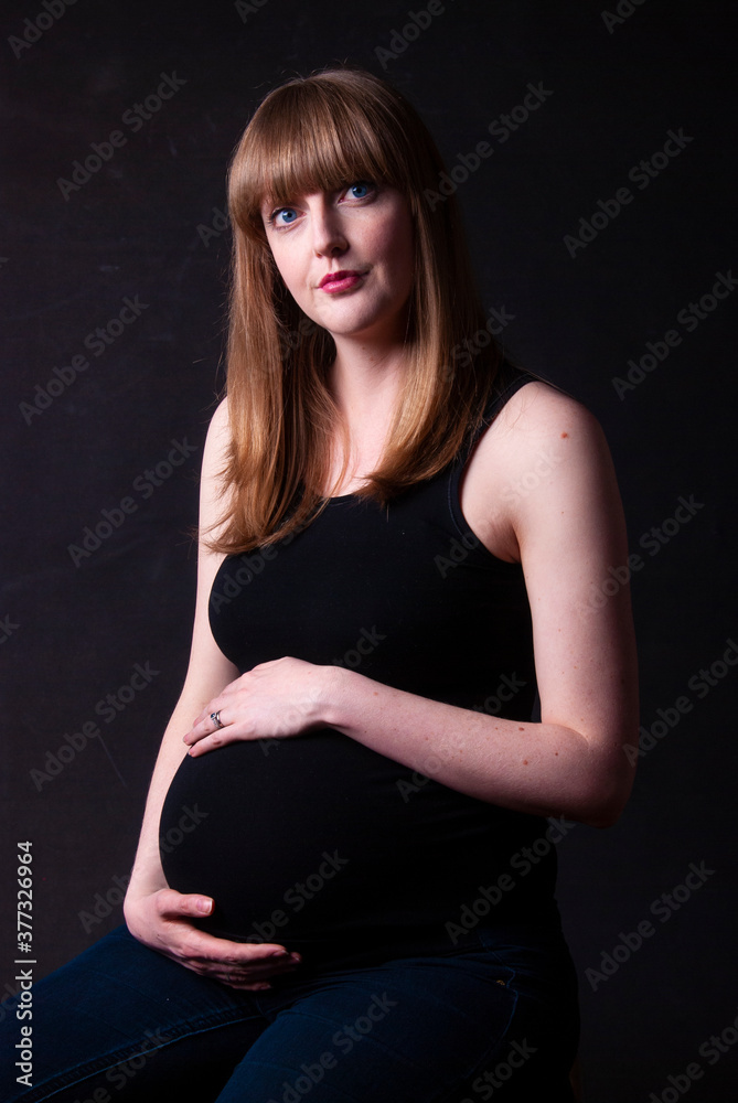 Portrait of a thoughtful pregnant woman with a black background, looking away from camera. Portrait of a thoughtful pregnant woman with a black background, looking away from camera.