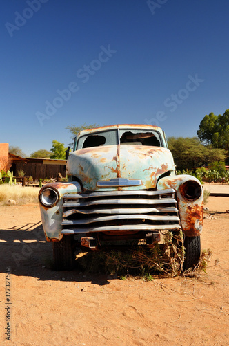 Rusty old car wreck abandoned in the African desert. Portrait format.