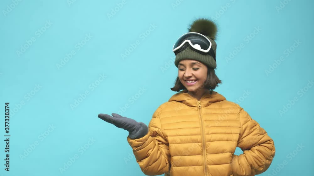Young snowboard indian woman showing a copy space on a palm and holding another hand on waist Young snowboard indian woman showing a copy space on a palm and holding another hand on waist
