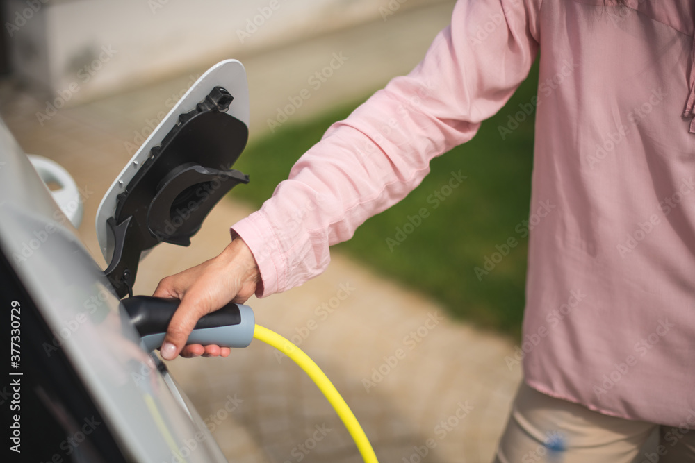Close up of a woman's hand charging a electric car at a charging station Close up of a woman's hand charging a electric car at a charging station