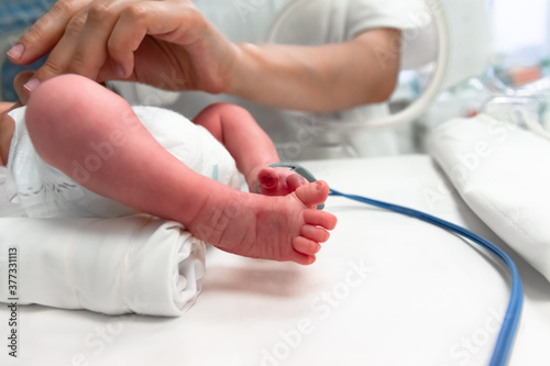 Nurse takes action to monitor and care for premature baby  selective focus - newborn baby foot with a neonatal pulse oximetry monitor and nurse arm. Newborn is placed in the incubator. Neonatal ward
