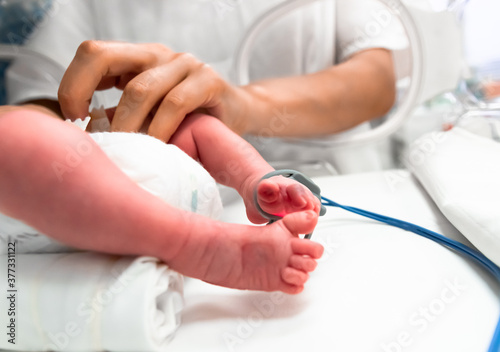 Nurse takes action to monitor and care for premature baby, selective focus - newborn baby foot with a neonatal pulse oximetry monitor and nurse arm. Newborn is placed in the incubator. Neonatal ward