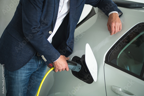 Man leaning against car holding a electric car charger © TheSupporter