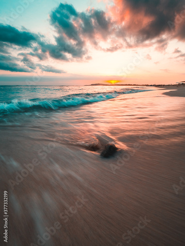 Ocean sunset, slow shutter, waves washing in over the sand. Strong sunset colors and clouds over the horizon