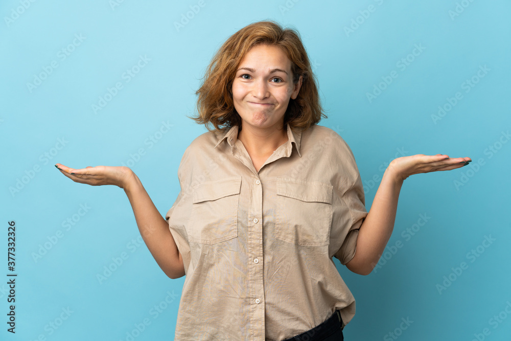 Young Georgian woman isolated on blue background having doubts while raising hands Young Georgian woman isolated on blue background having doubts while raising hands