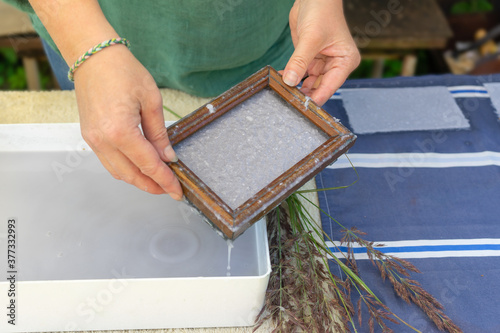 Woman holding frame for making paper sheets from waste paper pulp. Selective focus. Decorative and applied art. Recycling concept, ecology.