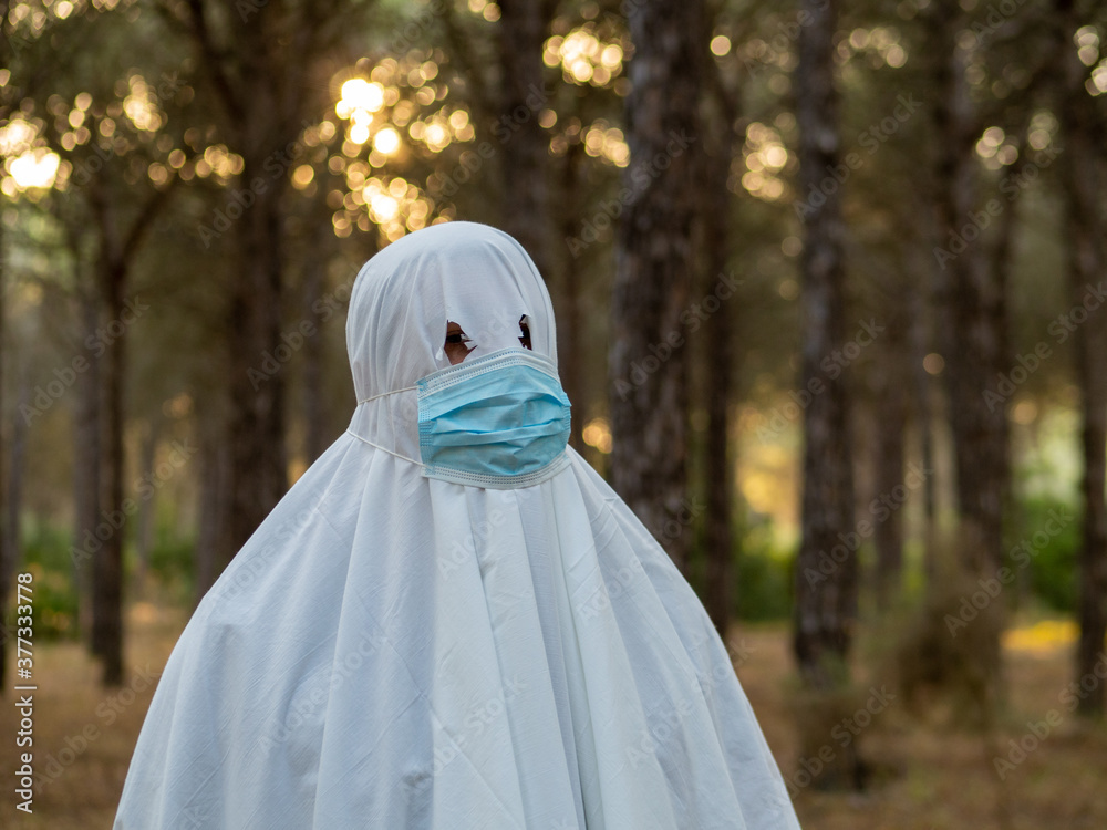 Hombre joven disfrazado de fantasma con mascarilla sanitaria celebrando halloween durante la pandemia del coronavirus Hombre joven disfrazado de fantasma con mascarilla sanitaria celebrando halloween durante la pandemia del coronavirus