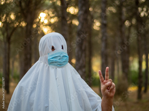 Hombre joven disfrazado de fantasma con mascarilla sanitaria celebrando halloween durante la pandemia del coronavirus