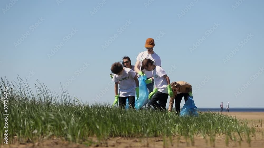 volunteers are walking on sand beach and collecting waste from ground, put in plastic bags Spbi. people and children in activist t-shirt clean river coast. family, community concept