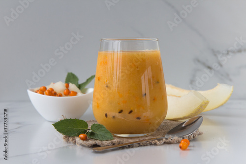 Glass cup with fresh melon and sea buckthorn smoothi on a light background. photo