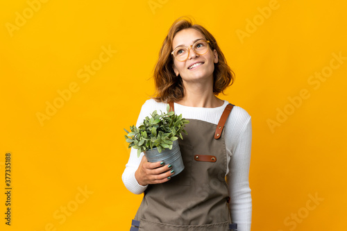 Young Georgian woman holding a plant isolated on yellow background thinking an idea while looking up