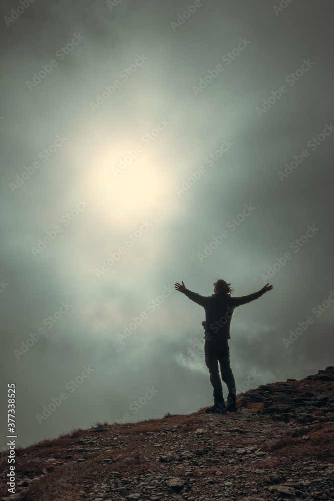 Man silhouette standing in front of sun and fog on the mountain