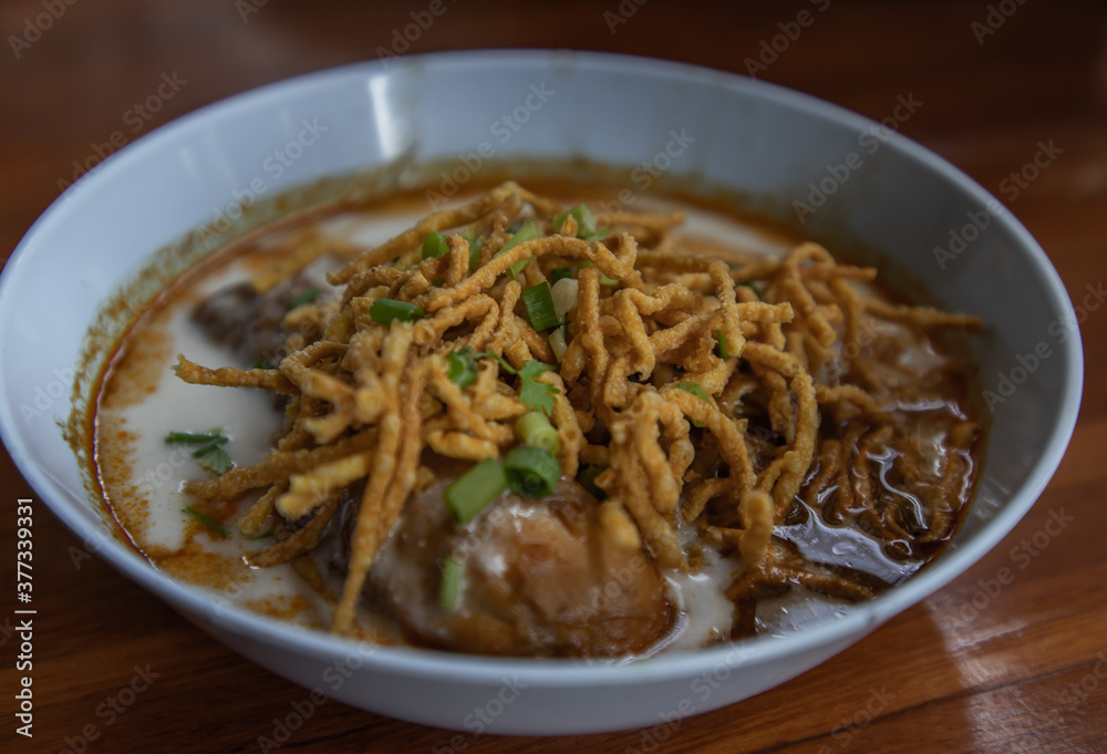 Traditional Khao Soi Recipe, Thai Northern Style Curried Noodle Soup with Chicken in white bowl. Selective focus. Traditional Khao Soi Recipe, Thai Northern Style Curried Noodle Soup with Chicken in white bowl. Selective focus.