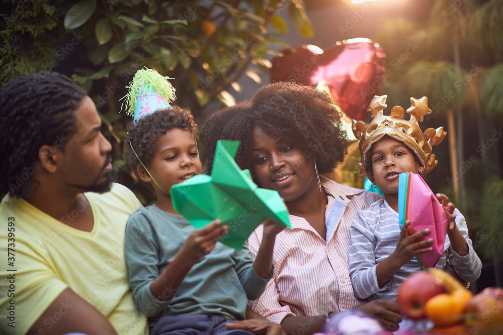 Fototapeta premium afro-american family gathered on birthday party playing with paper hat and boats