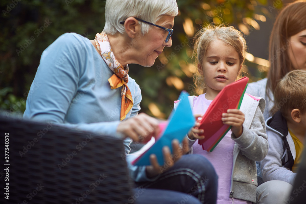 Εκτύπωση καμβά grandma is playing with granddaughter with paper boats sitting outside, focused